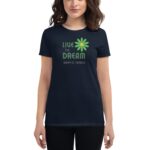 A woman wears a dark t-shirt featuring a floral design with the text "LIVE THE DREAM HAPPY ST. PATRICK" prominently displayed in green and yellow.