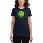 A person wears a dark t-shirt featuring a bright green smiley face graphic with the text HAPPY FACE above it in a playful font against a plain background.
