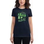 A person is wearing a navy t-shirt featuring a whimsical green graphic that reads "TAKE IT EASY" surrounded by small stars and two abstract shapes  creating a relaxed vibe.
