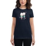 A woman wears a dark t-shirt featuring a cartoon design of a couple surrounded by pink hearts. She has wavy hair and a neutral expression  with her arms relaxed at her sides.