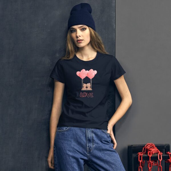 A woman wearing a black t-shirt with a graphic of cartoon animals holding pink balloons stands against a dark textured wall with a chain and box nearby.