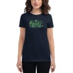 A woman wears a dark shirt featuring green text that reads "Happy St. Patrick's Day" along with shamrock graphics in a casual indoor setting.