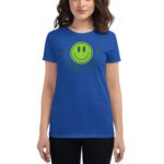 A woman stands wearing a bright blue t-shirt featuring a green smiley face graphic with the text HAPPY FACE above it in a playful style.