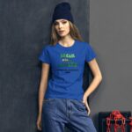 A woman stands confidently in a blue t-shirt that reads DREAM without LIMITS HAPPY ST PATRICKS 2024 against a dark textured background with a chain and red object nearby.