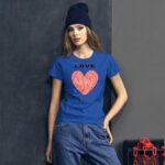 A young woman stands against a textured grey wall wearing a bright blue shirt featuring a red heart with fingerprint designs and the word LOVE above it. She has long hair and a dark beanie.