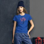 A woman wearing a bright blue t-shirt with a tree design in hearts stands confidently against a dark wall while wearing a dark beanie and casual jeans.