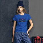 A woman stands against a textured gray wall wearing a blue t-shirt with the text "LOVE YOU" and a quote below it. She has long hair and is wearing a dark beanie.