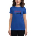 A woman stands wearing a blue t-shirt with the text "Valentines Babe" in red and black letters  surrounded by small hearts  against a plain background.