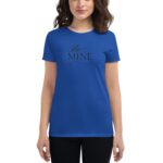 A woman wears a bright blue T-shirt displaying the text Be Mine in cursive font with hearts  standing against a plain background  presenting a casual and playful style.