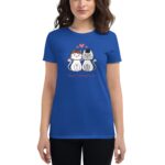 A woman wearing a blue t-shirt displays a graphic of two cartoon cats  one adorned with a floral crown  with the text "Happy Valentine's Day" underneath. Red hearts appear above them.