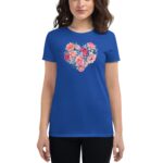 A woman wears a blue t-shirt adorned with a heart-shaped floral design featuring various colorful flowers against a plain background  showcasing a casual style.