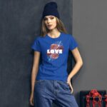 A model stands confidently against a dark wall wearing a vibrant blue t-shirt with a floral design and the word LOVE prominently featured while sporting a dark beanie and relaxed jeans.