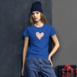 A young woman stands confidently against a dark wall wearing a blue t-shirt adorned with a heart graphic and text reading Happy Valentine’s Day styled with casual denim pants and a beanie.
