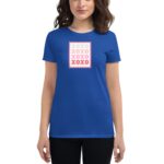 A woman stands wearing a blue t-shirt featuring a stamp design with the text XOXO in varying colors of pink and gray  set against a simple background.