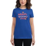 A woman wears a blue t-shirt displaying the text "HAPPY VALENTINE'S DAY" surrounded by flowers  standing against a neutral background  conveying a festive and cheerful mood.