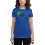 A woman wears a blue t-shirt featuring a green heart design with the text "Happy St. Patrick's Day" and a shamrock  standing against a plain background.