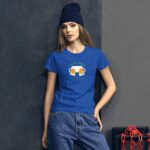 A woman wearing a blue t-shirt with a beer graphic stands confidently against a dark textured wall. She is styled with a knit beanie and casual jeans.