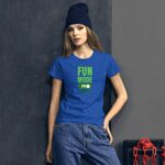 A young woman stands against a textured gray wall wearing a blue t-shirt with green text that reads FUN MODE ON paired with loose jeans and a dark beanie  creating a casual look.