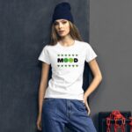 A young woman poses against a dark gray background wearing a white t-shirt with the word "MOOD" and a sad face graphic surrounded by green clovers  styled with jeans and a beanie.