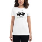 A woman wearing a white t-shirt with a smiling face graphic and sunglasses holds her hands at her sides in a casual setting. Text below the graphic reads LUCKY DAY.