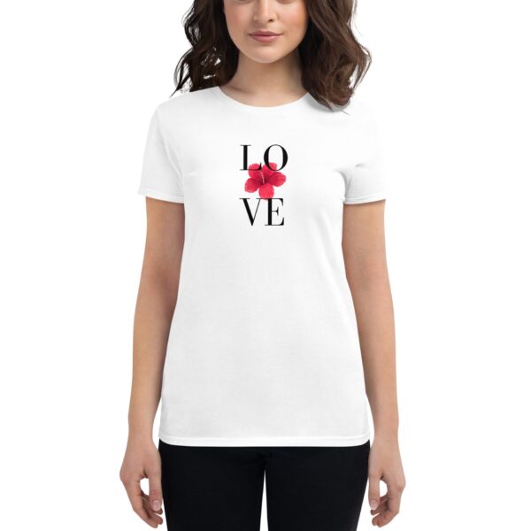 A woman wears a white t-shirt featuring the word "LOVE" in black letters with a red flower integrated into the design  standing in a neutral background.