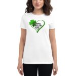 A woman wears a white t-shirt featuring a green heart design with a shamrock and text that reads Happy St. Patrick's Day emphasizing a festive celebration in a casual setting.