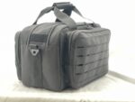 A black fabric bag rests on a flat surface featuring multiple zippered compartments and a textured design with rectangular cutouts it suggests utility and storage options against a light background.