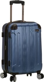 A blue hard-shell suitcase stands upright with a retractable handle and four wheels showcasing the brand Rockland on a textured surface suitable for travel settings.