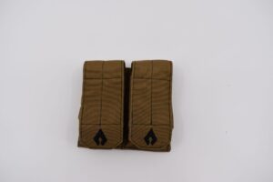 A brown tactical pouch with two compartments rests flat on a white surface displaying a sleek design with black emblem details and reinforced stitching designed for carrying equipment in rugged conditions.