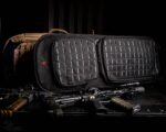 Two tactical bags are displayed side by side on a dark surface surrounded by two rifles and accessories showcasing a military or defense context emphasizing preparedness and functionality.