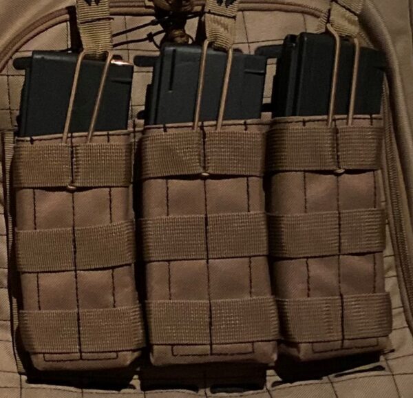 Three black magazines are secured within tan fabric pouches on a tactical vest background showcasing a grid pattern indicating military or outdoor equipment in a low-light setting.