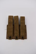 Three tan weapon magazine pouches are aligned vertically on a flat surface featuring a fabric backing with black insignia and stitched details in a clean and uncluttered environment.