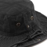 A black bucket hat rests on a surface featuring a round top and a wide brim with ventilation eyelets and an adjustable chin strap suggesting outdoor or casual use.