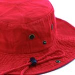 A red bucket hat features eyelets for ventilation and a cinch cord for adjustment resting on a flat surface against a white background.
