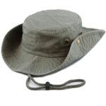 A wide-brimmed hat rests on a flat surface with a chin strap attached the hat's fabric is olive green featuring brass eyelets and a textured pattern designed for outdoor use