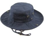 A navy blue bucket hat rests on a white surface featuring a round crown and a wide brim with ventilation holes and an adjustable chin strap for secure wear.