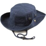 A navy blue bucket hat sits on a flat surface featuring a round top and wide brim with snaps on the side and an adjustable chin strap.