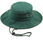 A green bucket hat sits on a flat surface with a wide brim and a drawstring for adjustment featuring small ventilation grommets on the sides showcasing a casual outdoor accessory.