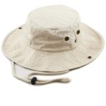 A beige bucket hat sits on a flat surface featuring a wide brim and ventilation eyelets with a drawstring for securing it during outdoor use.