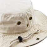 A beige bucket hat sits flat with metal ventilation eyelets and a cord with a toggle for adjustment highlighting its casual outdoor style suitable for sun protection.