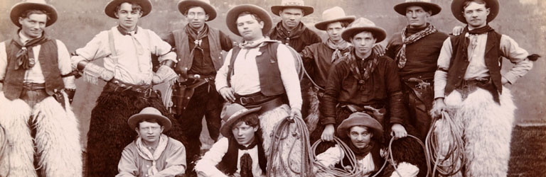 A sepia-toned photo of eleven cowboys in wide-brimmed hats, chaps, and bandanas, some holding ropes. They pose confidently, evoking a rugged, Old West vibe.