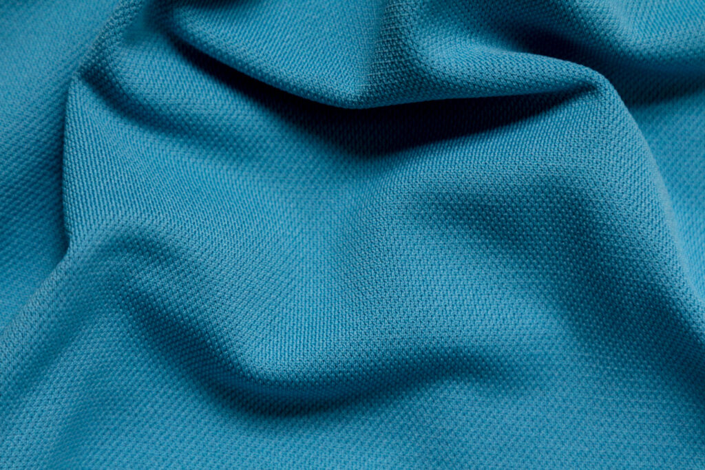 A full frame image of bright blue polyester fabric that is wrinkled. The material is simply composed with shadows below the ripples in the material.  The fabric is used for wicking sports applications.