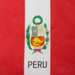 A flag featuring vertical red stripes on the sides and a white center displays the national coat of arms that includes a llama and a vicuña surrounded by greenery with the word PERU beneath it