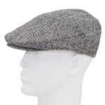 A flat cap sits atop a white mannequin head facing right showcasing a herringbone pattern in gray and black the background is plain and uncluttered