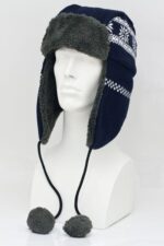 A navy winter hat with ear flaps and fuzzy lining sits on a mannequin head two decorative pom-poms hang from the chin straps showcasing a snowy pattern on the fabric