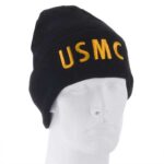 Black beanie hat displaying the text USMC in yellow letters is positioned on a plain white mannequin head against a neutral background. The hat symbolizes military affiliation.