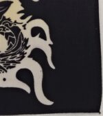 A black cloth features a white stylized design of a creature with flowing elements and intricate details suggesting movement amid a simplistic backdrop emphasizing the art's contrast and texture.