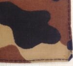 A piece of fabric featuring a camouflage pattern displays various shades of brown and black shapes intertwined against a lighter background with visible stitching along the edges.