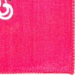 A vibrant pink fabric features a white circular design in the top left corner against a textured background with visible stitches along the edge. The setting appears to be a close-up view.