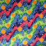A vibrant textile features a wavy pattern with bright yellow suns and varied stars set against a background of blue green and red shades creating a lively cosmic scene.